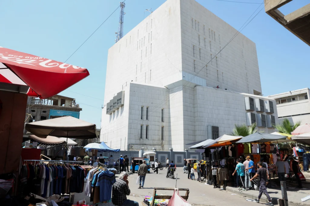 شحنات الدولار الأمريكي إلى العراق تكشف عن تحول هيكلي في النظام المصرفي A large white central bank building towering over a bustling street market in Baghdad, illustrating how US dollar shipments to Iraq impact financial stability and structural banking shifts.