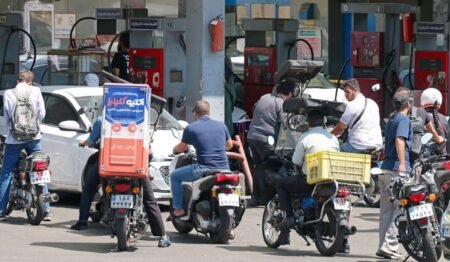 A crowded gas station in Tehran showing long queues of motorcycles and cars waiting at red fuel pumps, with drivers standing idle beside their vehicles, visually representing the severe fuel shortages and public frustration that embody the deepening Iran Economic Crisis as Washington maneuvers for a strategic endgame.