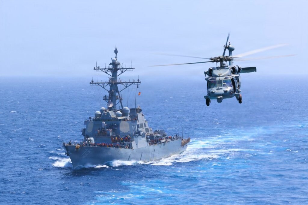 الضغط الاقتصادي الذي يمارسه ترامب يُجبر طهران على الدخول في حالة شَكّ A U.S. Navy destroyer and military helicopter conduct patrol operations in open waters, reflecting the naval enforcement backing Trump Economic Pressure.