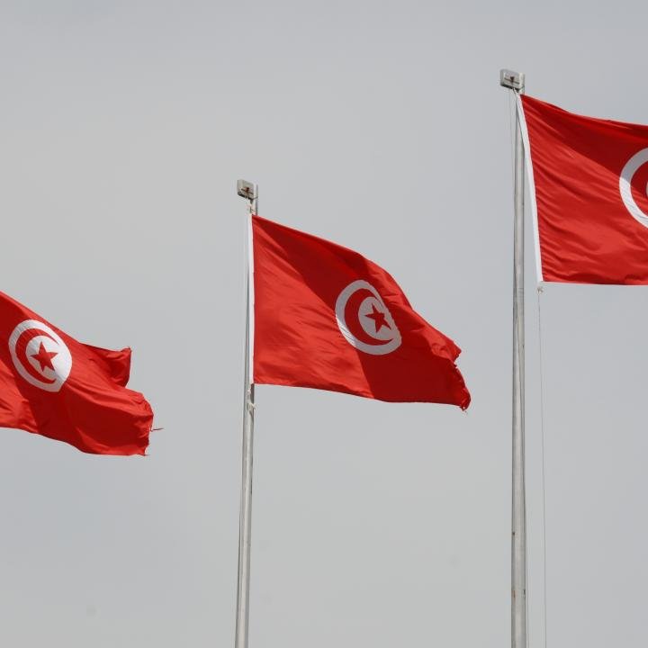 Five Years After Saied’s Power Grab, Tunisia Is Isolated and Unmoored National flags of Tunisia waving on tall flagpoles against an overcast sky, reflecting political isolation five years after Saied's Power Grab.