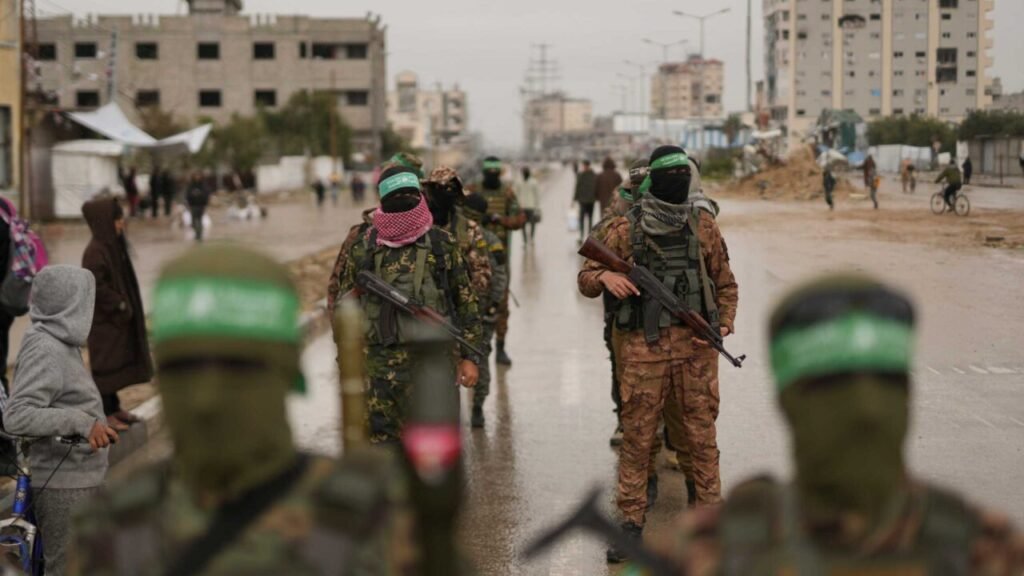 A street-level photograph capturing masked Hamas fighters in camouflage tactical gear and distinctive green headbands standing guard with assault rifles on a wet, overcast road in a war-torn urban neighborhood, with blurred civilians and a child in the foreground passing by, setting the tense ground-level scene that underscores the critical challenges facing the proposed Hamas Disarmament Roadmap, as the stark presence of armed militants highlights the deep obstacles to achieving a peaceful Gaza standoff.