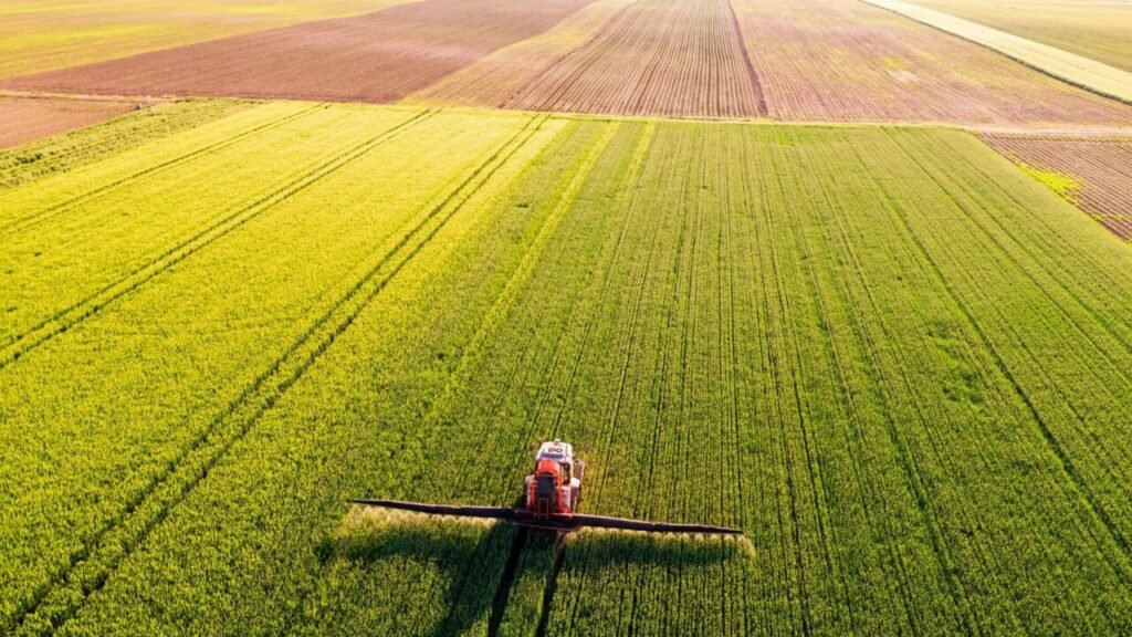 Aerial view of a tractor fertilizing crops, supporting US food security and agricultural supply chain resilience.