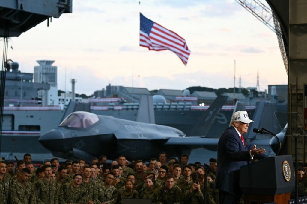 "President Donald Trump addresses a large crowd of US Navy personnel from a podium on the flight deck of the aircraft carrier USS George Washington, with a sleek F-35 fighter jet stationed behind him and an American flag waving prominently in the twilight sky, visually embodying the projection of overwhelming conventional military force whose operational effectiveness and strategic relevance are increasingly tested by the asymmetric vulnerabilities inherent in modern US Military Interventions."