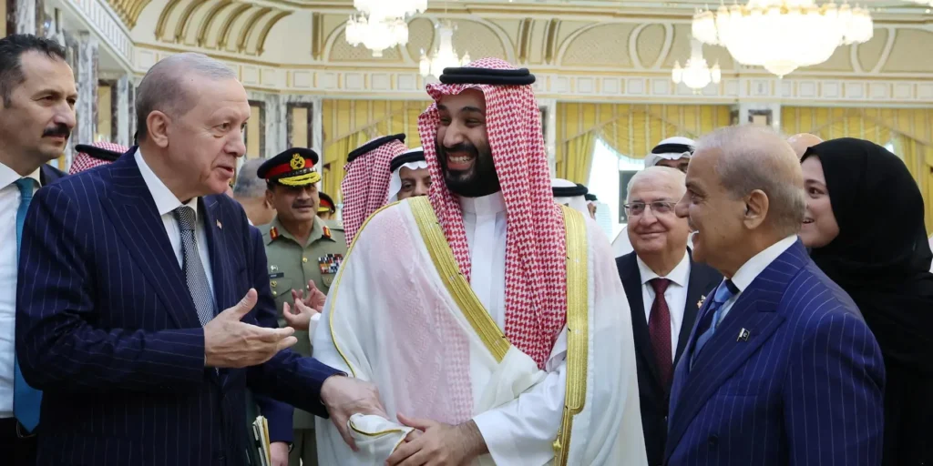 A high-level diplomatic photograph showing Turkish President Recep Tayyip Erdoğan, Saudi Crown Prince Mohammed bin Salman in traditional red-and-white shemagh and gold-bordered bisht, and Pakistani Prime Minister Shehbaz Sharif sharing a warm, lighthearted moment in a lavish palace hall, visually representing the ongoing regional rapprochement that suggests The Mecca Pact could strategically open new diplomatic pathways for Iran to re-engage with key Sunni powers and de-escalate lingering geopolitical tensions.