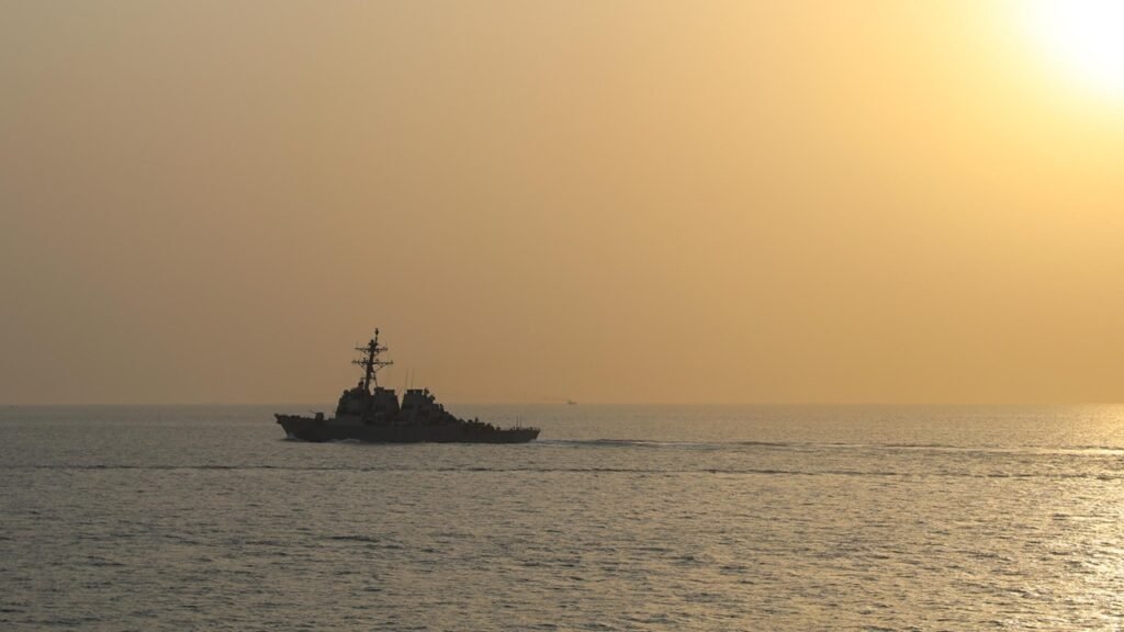 US warship transiting the Strait of Hormuz at sunset, illustrating Middle East chokepoints and Iran Maritime Strategy.