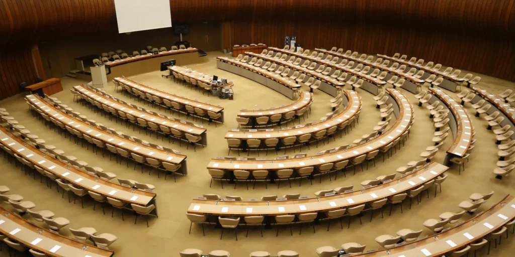 An empty semicircular conference hall with rows of desks and seats, representing international diplomacy where rising Middle powers will determine Middle East peace.