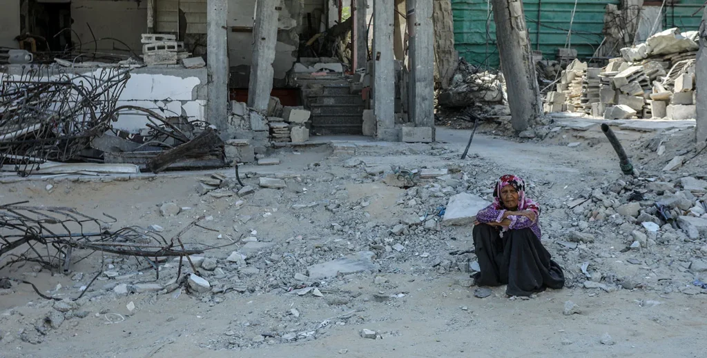 طرح گازای ترامپ نمایندگی ملی فلسطینیها را محو میکند Elderly woman sitting among destroyed buildings in Gaza, highlighting humanitarian impacts of the Trump Gaza Plan.