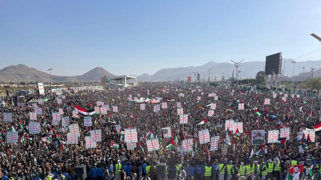 A massive crowd of demonstrators wave Palestinian flags and hold placards during a rally in Yemen, capturing the ideological mass mobilization behind the Houthis threat.