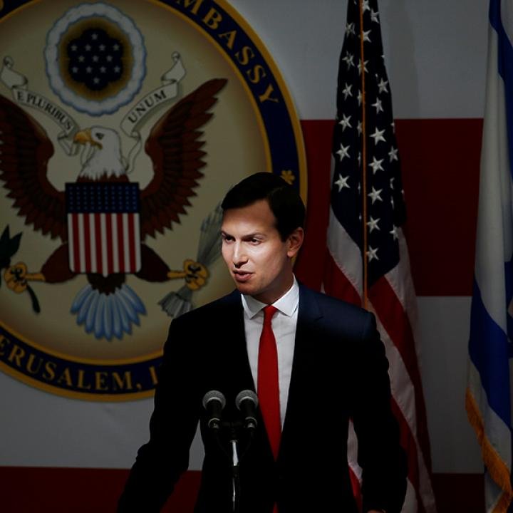 Gaza Security Drives Kushner Into High-Stakes Diplomacy A medium shot of Jared Kushner speaking into microphones at a press conference, standing in front of the official United States Embassy Jerusalem seal, flanked by the American flag and a partial view of the Israeli flag, visually capturing the high-stakes diplomatic setting where Gaza Security and regional stability are the focal points of his intensive geopolitical engagement.