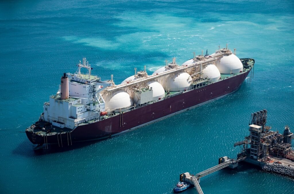 تنوع الاقتصاد القطري يتجاوز نمو الغاز An aerial view of a large LNG carrier with spherical tanks docked at a marine loading terminal, contrasting traditional gas exports with broader efforts toward Qatar Economic Diversification.