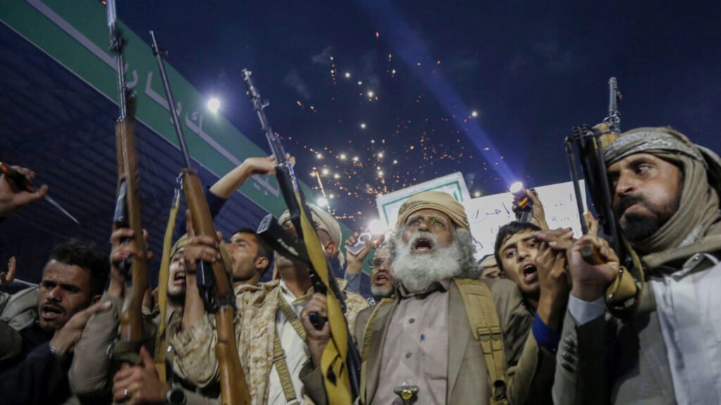 Armed Houthi supporters chant and raise rifles into the air during a night rally in Sanaa, highlighting how regional escalation in Yemen deepens the Saudi dilemma regarding the Iran war.