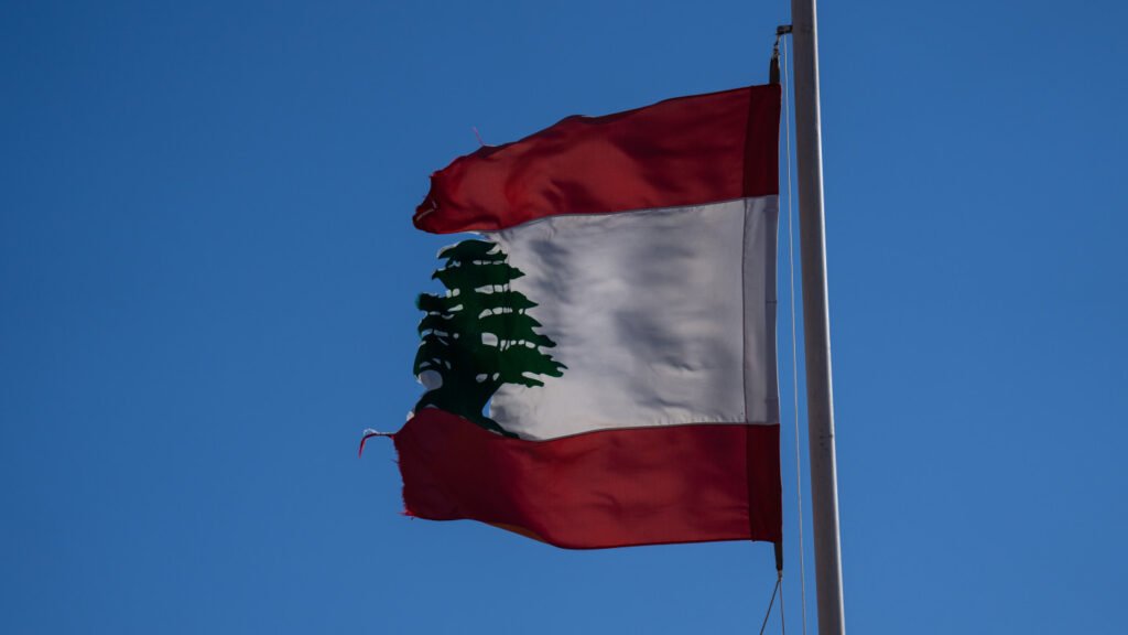 لغو مجازات اعدام سیستم عدالت لبنان را مورد آزمایش قرار میدهد A tattered, frayed Lebanese flag waving against a clear blue sky, symbolizing the fragile and strained state of the nation's legal institutions as the contentious debate over Death Penalty Abolition puts Lebanon's justice system to the ultimate test.