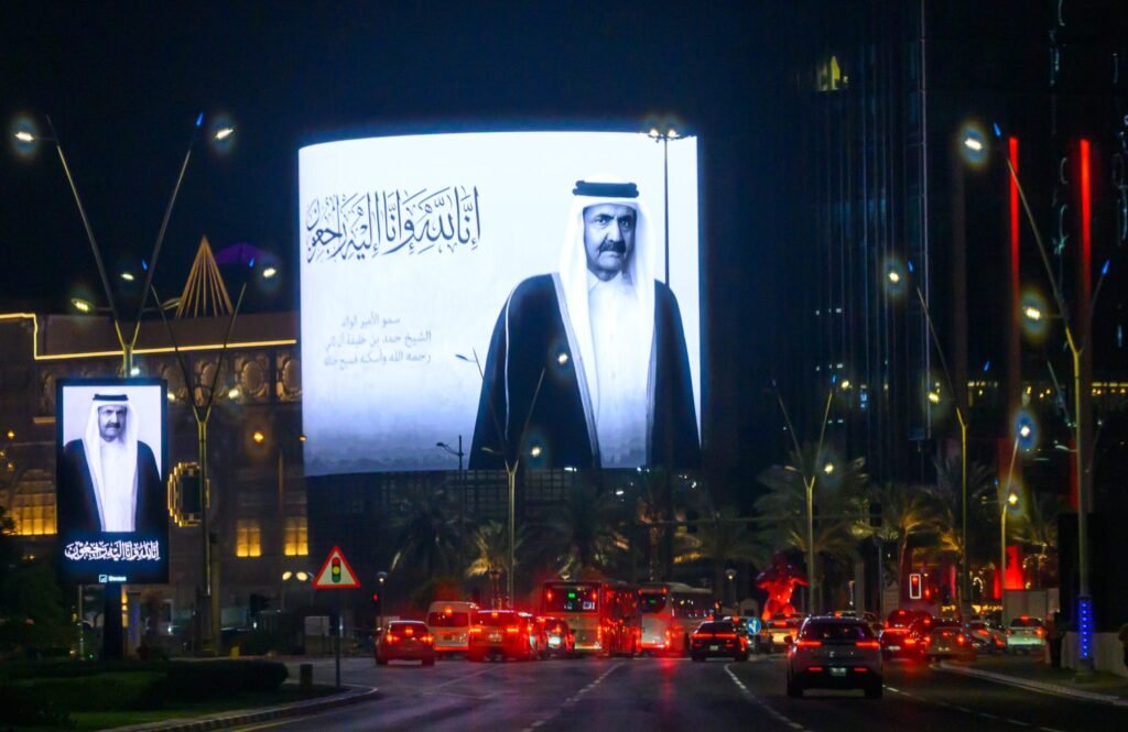 Modern Qatar Transformation Redefined Small State Power Digital billboards displaying former Emir Sheikh Hamad bin Khalifa Al Thani along a night-lit Doha street, illustrating the geopolitical transformation of Modern Qatar.