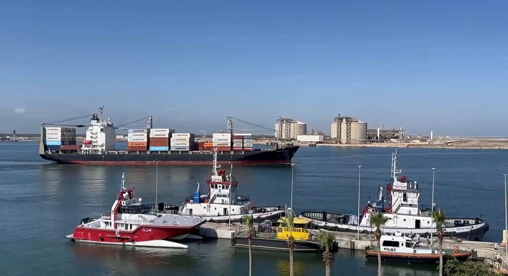 How Egypt Became the Middle East’s New Energy Chokepoint A large cargo container vessel and tugboats positioned near LNG storage tanks at Damietta port, illustrating Egypt's maritime infrastructure as a critical Energy Chokepoint in the Middle East.