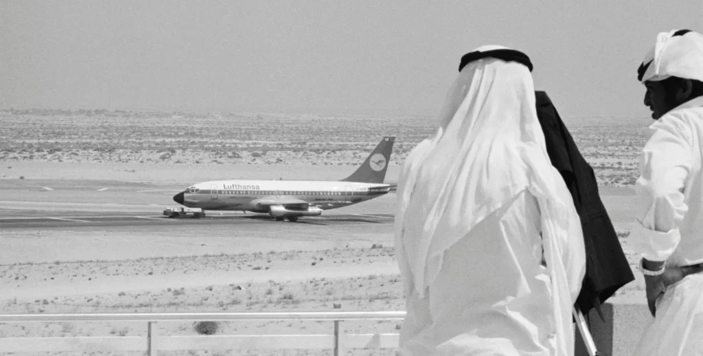 Middle East Revolutionaries Linked Marxists and Islamists Archival black-and-white photograph of men in traditional Arab dress observing a Lufthansa airliner on a desert tarmac, reflecting the historical tactics of Middle East Revolutionaries.