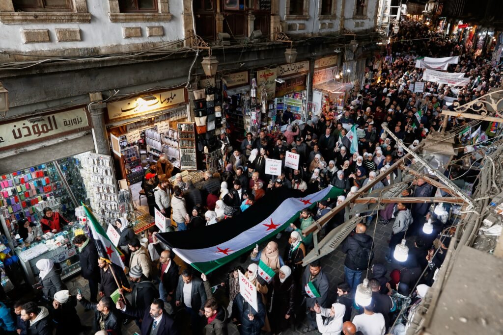 Syria strategy emerges as key to Middle East stability Demonstrators carry a large Syrian revolution flag through the Old City of Damascus during a march marking its 15th anniversary, reflecting internal political dynamics that shape a regional Syria strategy.