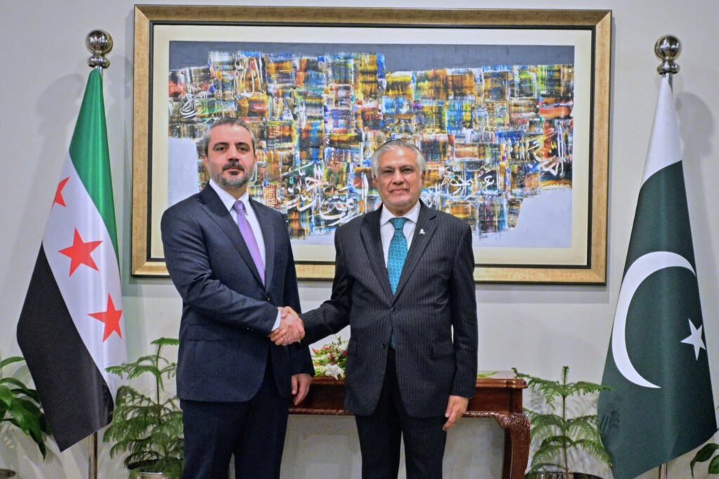 پیوستن سوریه به پیمان دفاعی سعودی-ترکی-پاکستانی، ریسکهای منطقهای را افزایش میدهد A formal photograph of Syrian Foreign Minister Asaad Hassan al-Shibani shaking hands with Pakistani Foreign Minister Ishaq Dar in Islamabad, flanked by the official Syrian and Pakistani flags, visually representing the high-level diplomacy driving the Syria defense pact accession, which significantly raises regional geopolitical stakes.