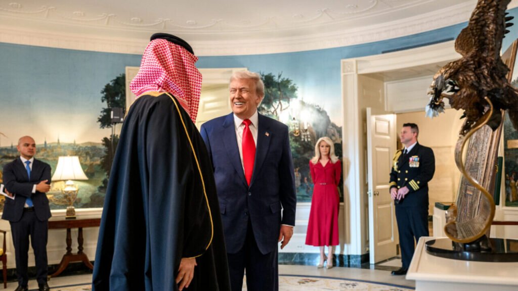 A formal photograph of President Donald Trump smiling and engaging warmly with Saudi Crown Prince Mohammed bin Salman (MBS), dressed in traditional red-and-white checkered headwear and a dark bisht, inside the White House Diplomatic Reception Room with Ivanka Trump and a military aide observing in the background, highlighting the high-level diplomatic negotiations that allow the Saudi nuclear program to advance and threaten US nonproliferation policy.
