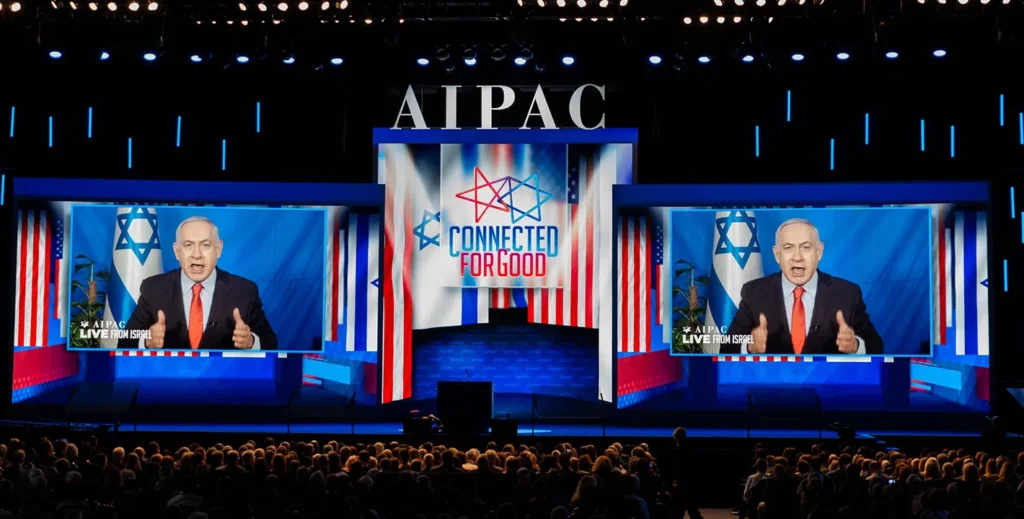 Israeli Prime Minister Benjamin Netanyahu addressing an audience via large video screens at an AIPAC conference stage, highlighting the political influence of the Israel Lobby.