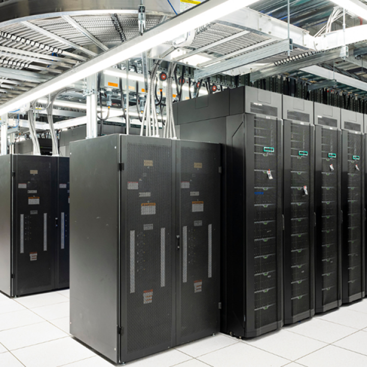 Saudi AI Ambitions Give Washington a Strategic Opening A photograph of a modern data center floor featuring tall, black server racks with dense cabling and overhead cable trays on a white tiled floor, symbolizing the massive computational infrastructure required for Saudi AI Ambitions that provides Washington with a critical strategic opening to leverage technological partnerships.
