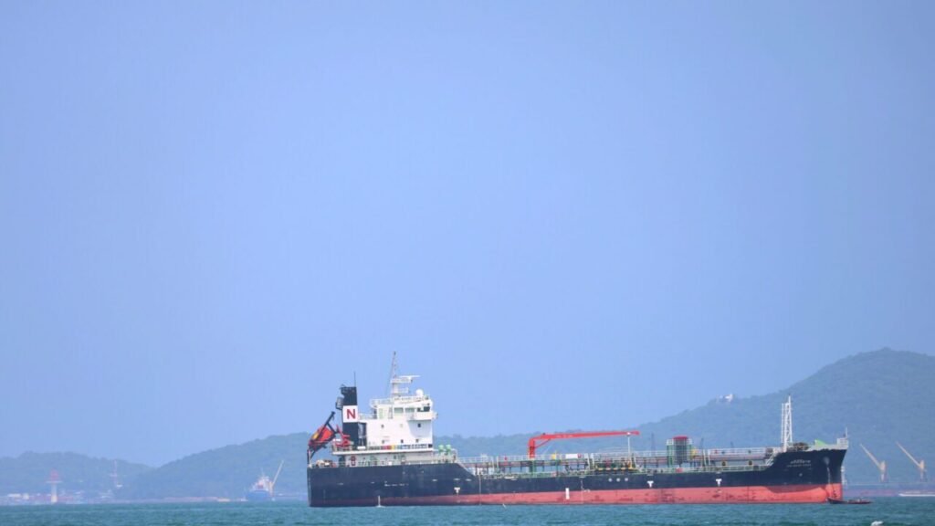 A photograph of a large red-and-black oil tanker sailing through the Bab el-Mandeb Strait off the coast of Yemen, with hazy mountains in the background, symbolizing the successful maritime pressure of the Houthi Victory that exposes the fundamental weaknesses of President Donald Trump's Iran strategy.