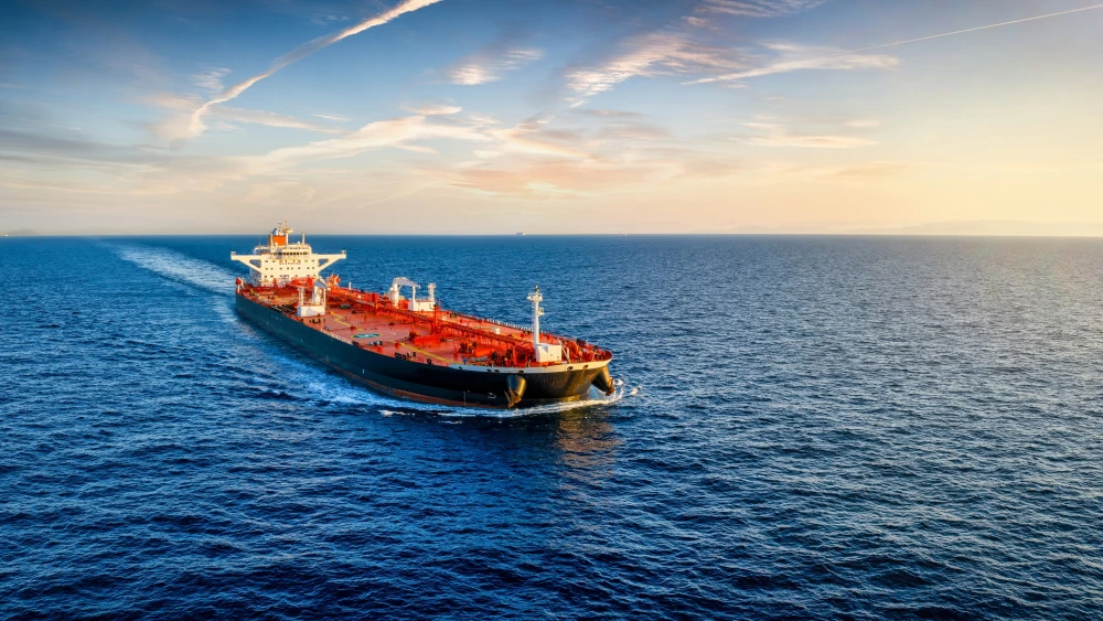 أسطول إيران الخفي يضعف بدون وقود وتأمين A photograph of a solitary large crude oil tanker with a dark hull and red deck sailing through open blue waters under a bright sky, leaving a wake, symbolizing the vulnerable and isolated state of the Iran shadow fleet that is increasingly weakening without essential fuel supplies and maritime insurance.