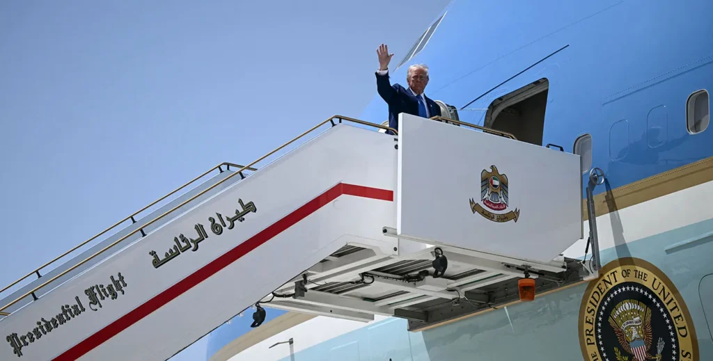 A high-angle photograph of US President Donald Trump waving from a white aircraft boarding staircase marked "Presidential Flight" in English and Arabic, featuring the UAE falcon emblem, while attached to Air Force One, symbolizing the departure and shifting alliances that characterize the US Mideast Exit, shattering the long-held myth of an enduring US security umbrella.