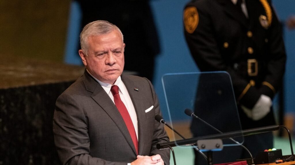 A solemn photograph of King Abdullah II of Jordan speaking at the UN General Assembly podium, with his hands clasped and a security guard in the background, symbolizing the intense regional pressure and political vulnerability that is fracturing the US-Jordan Alliance amid severe domestic backlash and direct Iranian targeting.