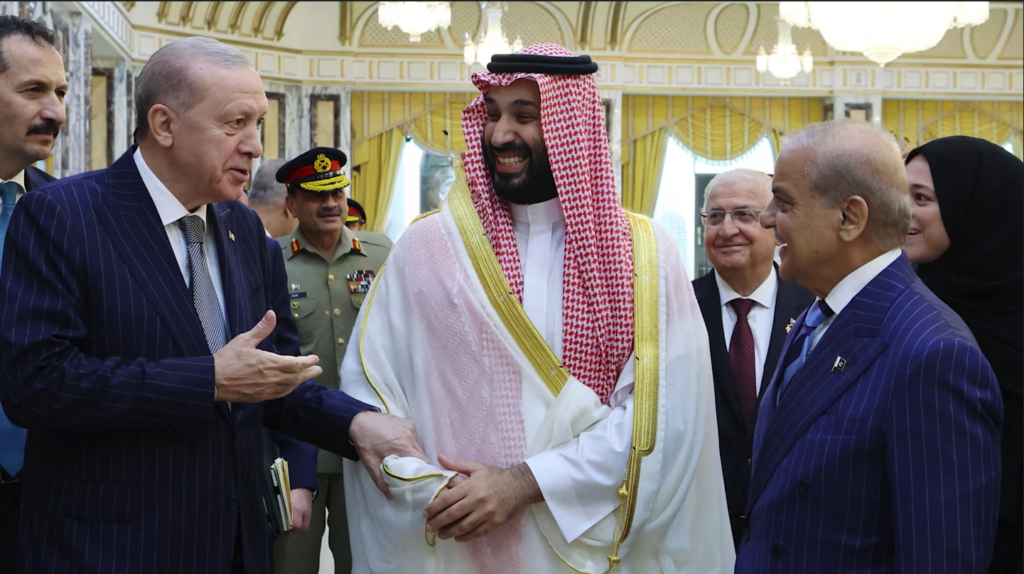 A warm diplomatic photograph showing Turkish President Recep Tayyip Erdoğan, Saudi Crown Prince Mohammed bin Salman in traditional red-and-white headwear, and Pakistani Prime Minister Shehbaz Sharif sharing a lighthearted moment in Mecca, symbolizing the strategic realignment forged by the Saudi Defense Pact that marks a bold shift beyond Washington's traditional security umbrella.
