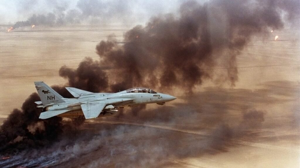 A historic photograph of a US Navy F-14 Tomcat fighter jet flying over the burning Kuwaiti oil wells during the 1991 Gulf War, with thick black smoke billowing from the desert below, symbolizing the military might that once defined the unipolar era but now fast-tracks US Power Decline as three Gulf wars drain its strategic dominance.
