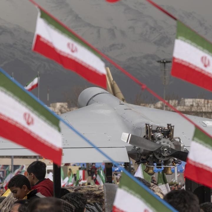 Iran Missile Rebuilding Creates a New Point of Failure A grey Shahed-type drone on display amid Iranian flags and a public crowd, highlighting the Iran Missile Rebuilding effort that creates a new point of failure.