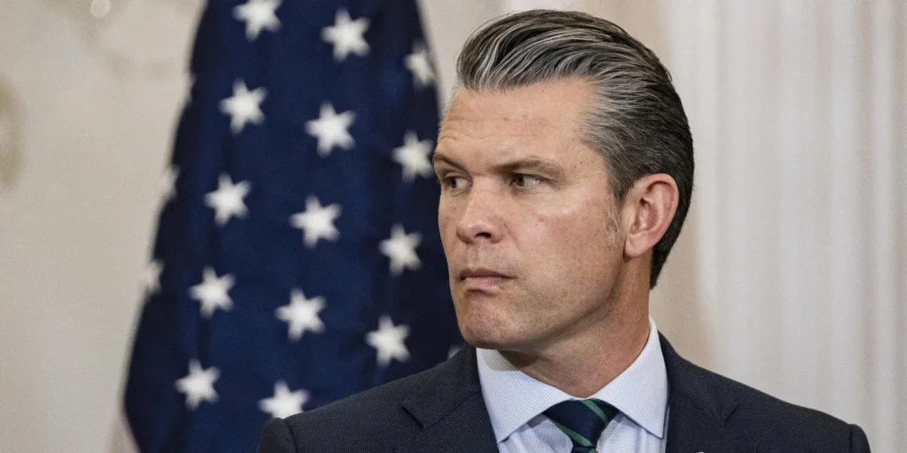 بيت هيغسث خدع ترامب بشأن حرب لا يمكنه الفوز بها Pete Hegseth in a dark suit and green tie with a US flag in the background, symbolizing how Hegseth misled Trump on a war he cannot win.
