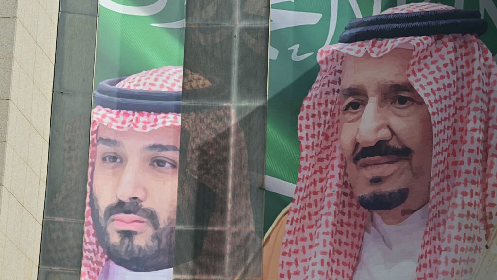 Two large portraits on a building show Saudi Crown Prince Mohammed bin Salman and King Salman in traditional red-and-white keffiyehs against green backgrounds, a scene reflecting the Saudi Two-Front Crisis that has handed Iran the upper hand.