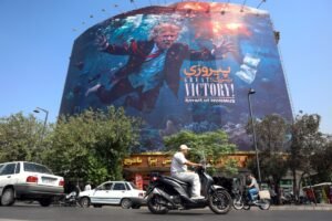 A vibrant street-level photograph of a massive billboard in Tehran showing a satirical underwater caricature of Donald Trump, dressed in a suit and red tie, drowning and flailing among fish in the Strait of Hormuz, emblazoned with "GREAT VICTORY!" and Persian text, symbolizing Tehran's propaganda celebrating the failure of the US Air Campaign due to its flawed and unrealistic aims.