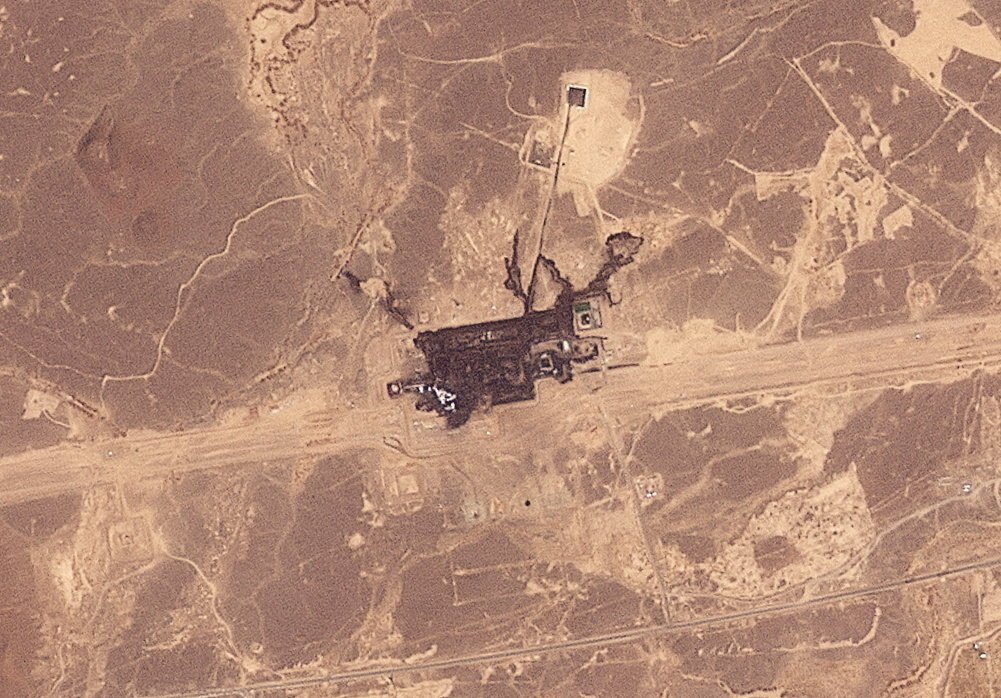 Saudi Oil Exports: Flexibility Finally Meets Its Limits A satellite view of a scarred industrial facility surrounded by arid desert in Saudi Arabia's Hejaz region, with dark burn marks spreading across the East-West pipeline complex — a stark image of the Saudi Oil Exports that are now meeting their limits.