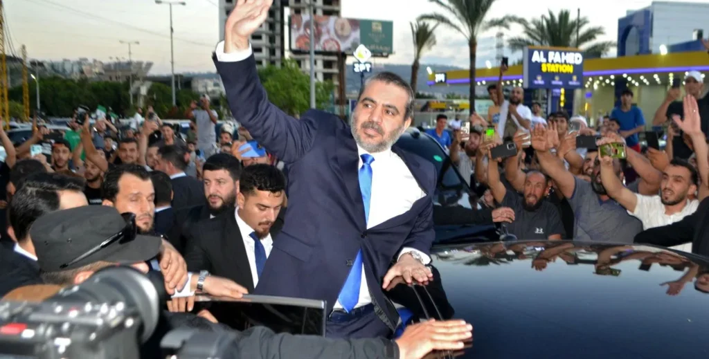 Syria-Lebanon relations shift from dominance to states A man in a blue suit and tie waves to a crowd from the sunroof of a black car as supporters raise their phones, capturing a public moment that reflects the shift in Syria-Lebanon relations from dominance to states.