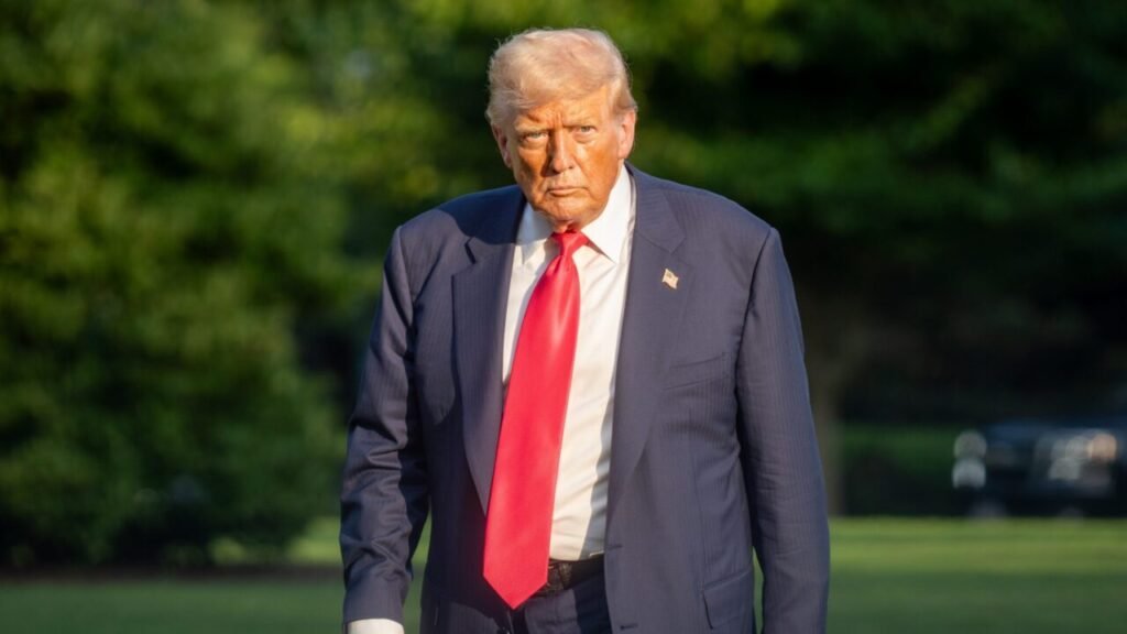 جنگ فرسایشی ایران استراتژی اقتصادی ایالات متحده را تضعیف میکند A photograph of a stern-looking President Donald Trump in a navy suit and red tie walking outdoors, his serious expression reflecting the mounting strategic frustration as the prolonged Iran War of Attrition defeats the US economic campaign strategy.
