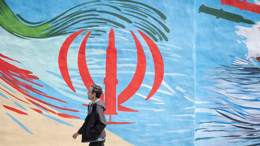 Man walking past a mural showing a missile-shaped Iranian emblem representing Iranian supersonic missiles.