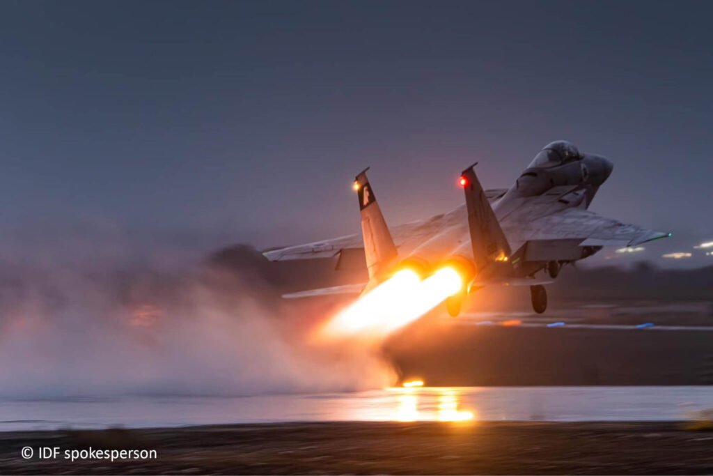 Iran Strategic Disruption, Not Victory, Is Israel’s Real Test A dramatic low-angle photograph of an Israeli Air Force F-15 fighter jet taking off from a wet runway at night, its blazing afterburners illuminating the thick fog and reflecting off the tarmac, symbolizing the sustained military campaign aimed at achieving Iran Strategic Disruption rather than a decisive victory, which is the real strategic test for Israel.