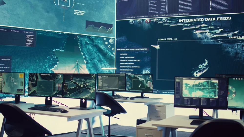Islamist Networks Thrive as US Misses the Threat A photograph of a modern military command center featuring multiple computer monitors displaying tactical maps, targeting data, and integrated surveillance feeds across a large wall screen, with empty chairs indicating a lack of active monitoring, symbolizing the sophisticated US intelligence apparatus that nonetheless fails to detect how Islamist Networks continue to thrive and evade detection.
