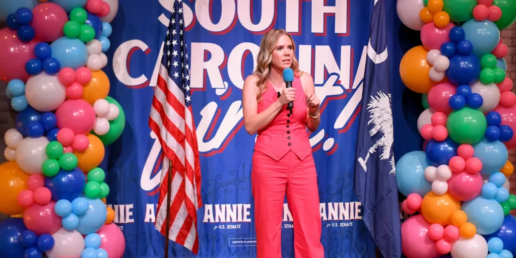 South Carolina Democratic Senate candidate Annie Andrews speaking into a microphone on stage during a campaign event, illustrating political shifts in adopting America First rhetoric.