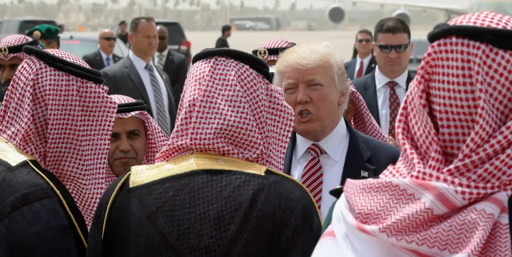 Donald Trump surrounded by Gulf officials in traditional headdresses on an airfield, symbolizing US defense policy and Trump arms sales.
