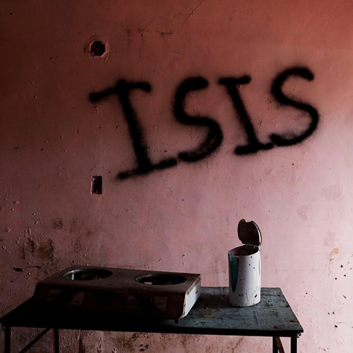 چرا بازیابی داعش وابسته به دستاوردهای ایران است، نه عقبنشینی آمریکا Black spray-painted graffiti reading "ISIS" on a damaged wall in a war-torn room above a small table with a stove burner, illustrating regional instability and the threat of an ISIS resurgence.