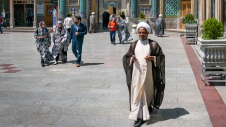 A cleric in traditional robes walks through a tiled courtyard, representing the Islamic Authority the West must stop deferring to.