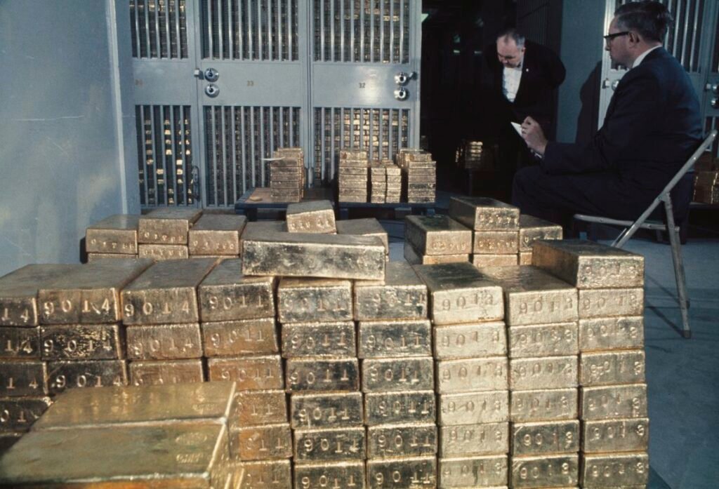 Stacks of gold bullion bars inside a secure bank vault with officials inspecting inventory, illustrating global reserve management and Gold repatriation.
