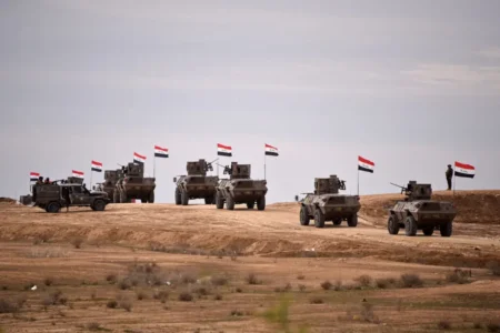 Iraqi military convoy flying national flags in the desert, highlighting the Withdrawal from Iraq and its effect on militias.