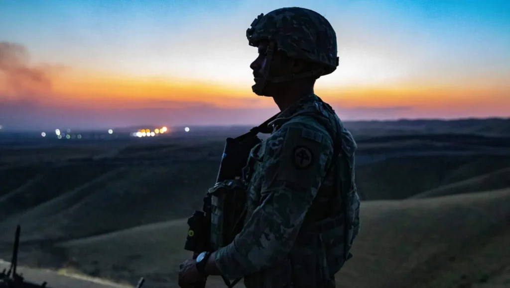US-Iraq Engagement Should Outlast Troop Withdrawal Silhouette of a soldier in combat uniform standing guard at dusk overlooking a distant outpost, symbolizing military drawdown and the future of long-term US-Iraq Engagement.