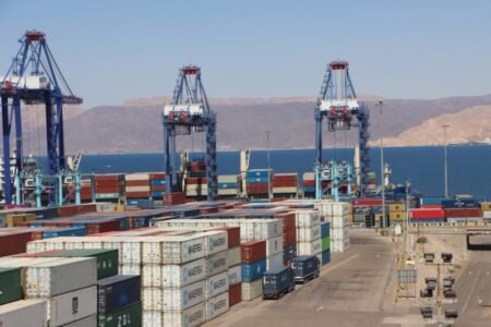 Commercial shipping containers stacked at the Port of Aqaba with gantry cranes operating along the Red Sea coast, demonstrating Jordan Economic Resilience amid regional shocks.