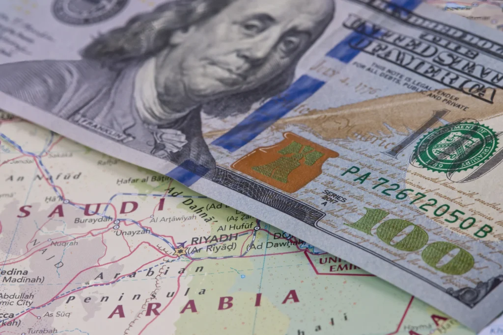 Gulf Dollar Peg Is the Real Vulnerability, Not Oil Invoicing A US $100 bill resting on a map of Saudi Arabia, illustrating the economic vulnerability of the Gulf Dollar Peg.