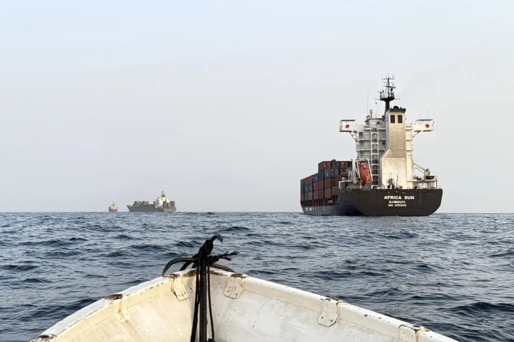 Commercial cargo and tanker ships navigating strategic maritime routes viewed from open water, highlighting security risks to Gulf Oil Exports through key chokepoints like Hormuz and Bab al-Mandab.